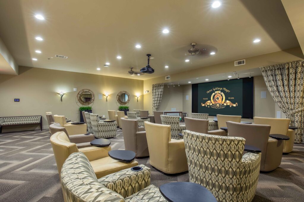 A movie theater room with light yellow, brown, and patterned sofa chairs positioned in front of the projector that's displaying the Metro Goldwyn Mayer lion intro.